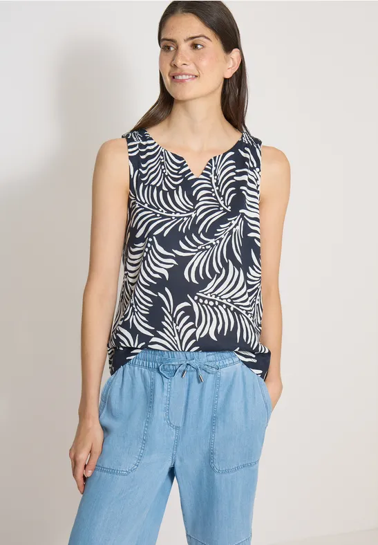 Femme porte un débardeur bleu marine à motifs de feuilles blanches et un pantalon en jean clair.