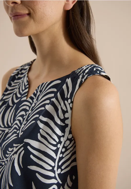 Une femme porte un top sans manches bleu foncé à motif de feuilles blanches.