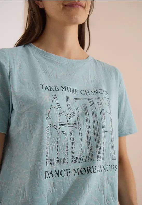 Dame in blauem T-Shirt mit 'Take More Chances, Dance More Chances' Schriftzug und Muster