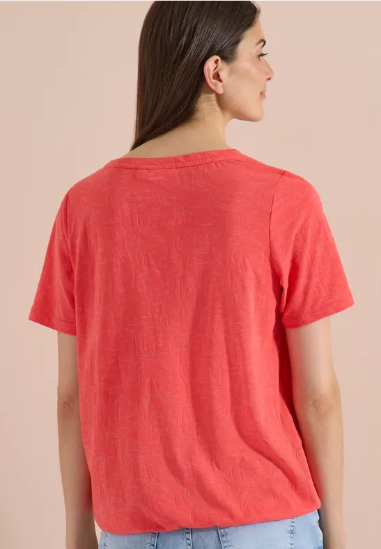 Rückansicht einer Person in einem korallefarbenen T-Shirt vor beigem Hintergrund.