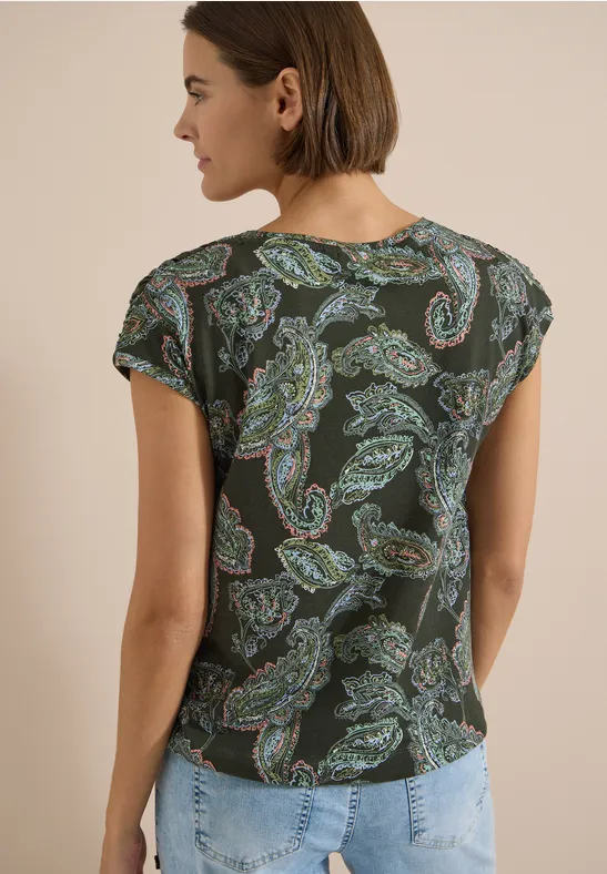 Frau von hinten in dunkelgrünem Paisley-Shirt und hellblauen Jeans.