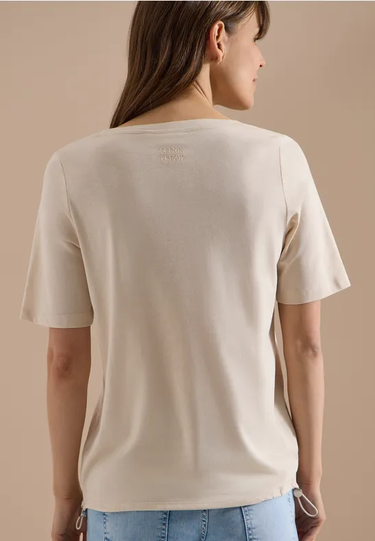Rückansicht einer Frau in lockerem beigem T-Shirt vor schlichtem Hintergrund.