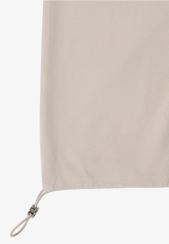 Beige Stoff mit Tunnelzug und verstellbarem Kordelstopper am unteren Rand.