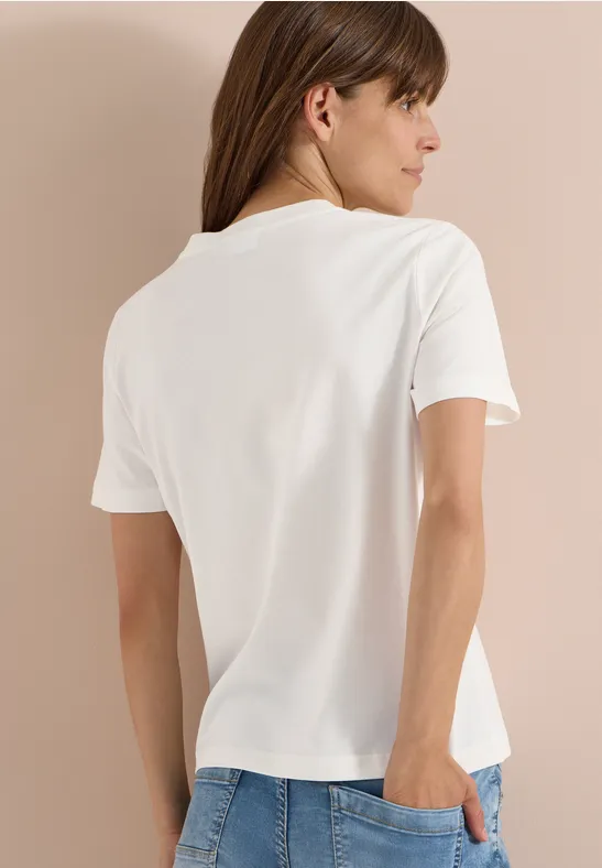 Rückansicht einer Person mit schlichten weißen T-Shirt vor beigem Hintergrund.