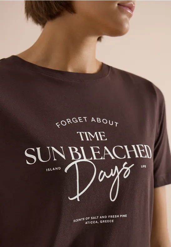 Braunes T-Shirt mit weißem Slogan 'Forget About Time. Sun Bleached Days.' getragen von einer Frau.