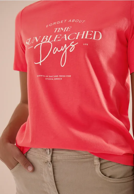 Rotes T-Shirt mit weißem Schriftzug "Forget about time unbleached days" und beiger Hose.