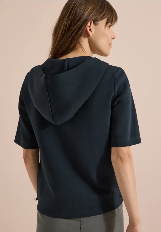 Frau trägt dunkelblaues Kapuzen-T-Shirt mit halblangen Ärmeln, Rückansicht.