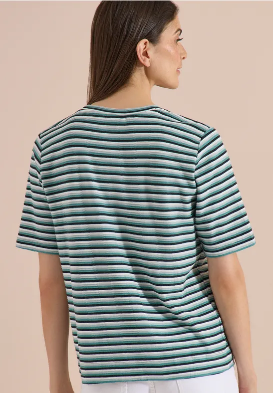 Frau von hinten in einem weiß-türkisen gestreiften T-Shirt vor beigem Hintergrund.