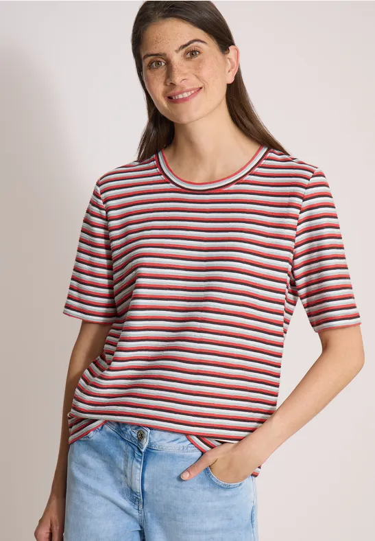 Frau in gestreiftem T-Shirt und Jeans vor hellem Hintergrund.