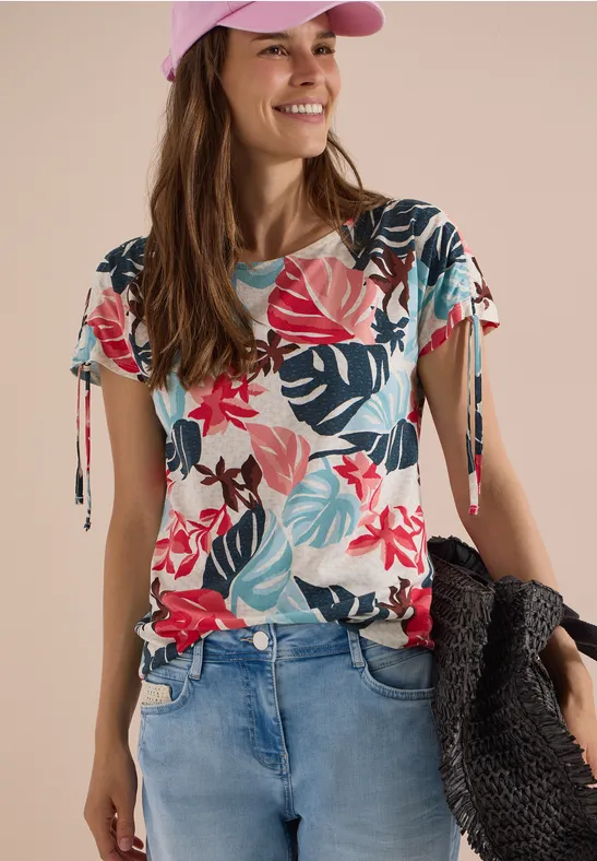 Femme en jean, t-shirt fleuri coloré et casquette rose, portant un panier noir.