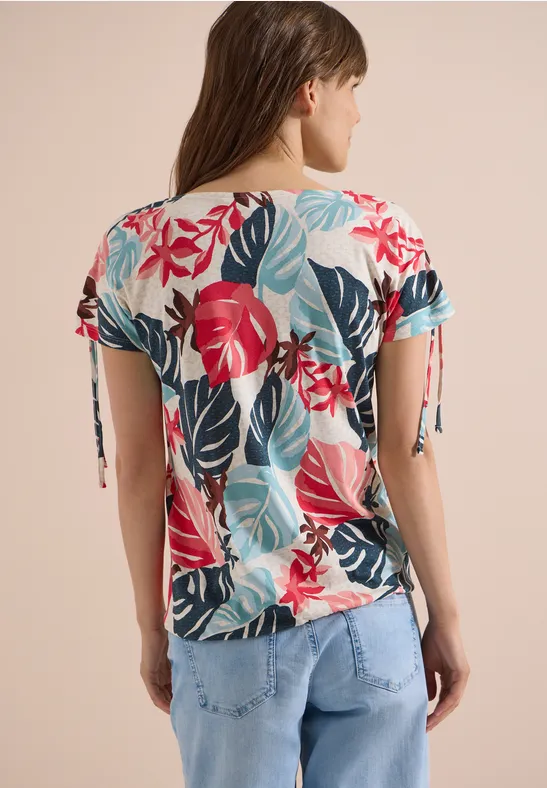 Femme de dos portant un top à manches courtes au motif tropical coloré et un jean clair.