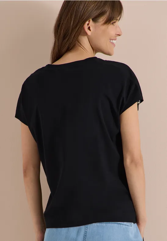 Frau von hinten in schwarzem T-Shirt und blauer Jeans vor beigem Hintergrund.