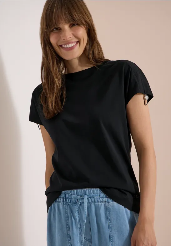 Person mit verschwommenem Gesicht trägt schwarzes T-Shirt und blaue Jeans.