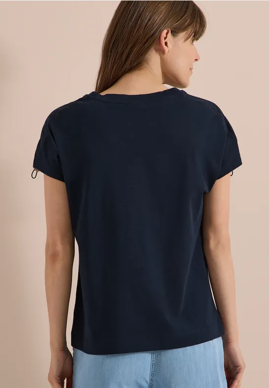 Rückansicht einer Frau in schlichten dunkelblauen T-Shirt vor neutralem Hintergrund.
