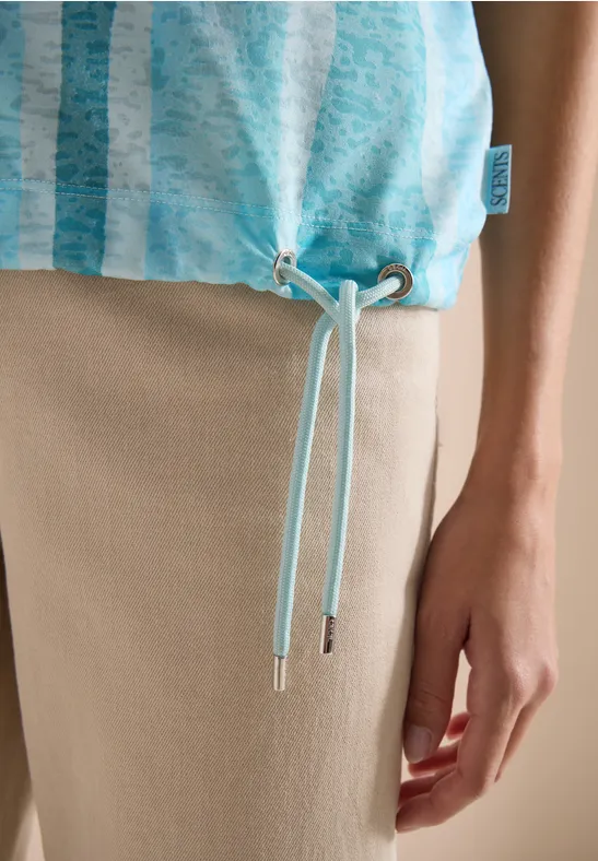 Top turquoise à fines rayures avec cordons de serrage au bas, porté sur pantalon beige.