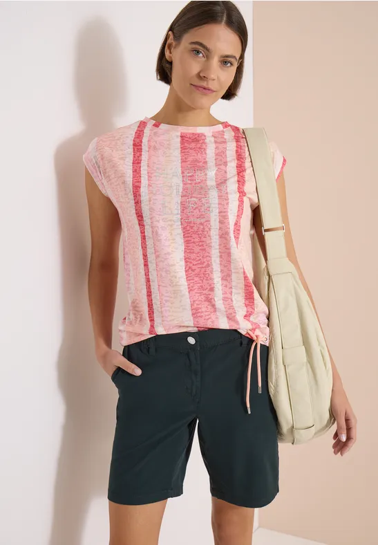 Femme en t-shirt à rayures rose et blanc, short bleu foncé et sac d’épaule.