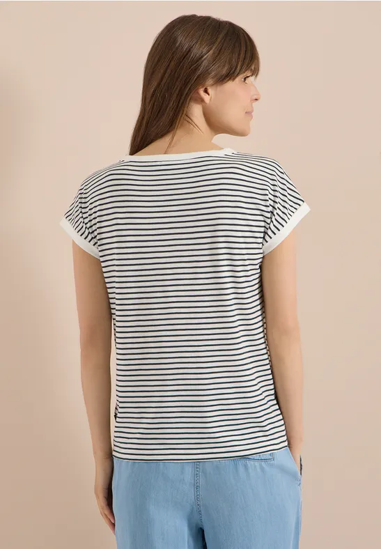 Rückenansicht einer Frau in weiß-schwarz gestreiftem T-Shirt und hellblauer Hose vor hellem Hintergrund.