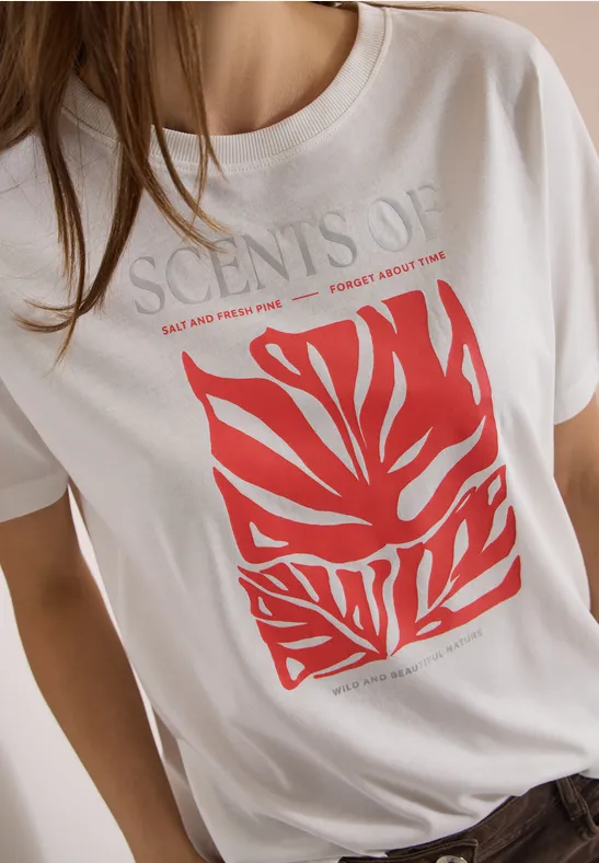 Jemand trägt ein weißes T-Shirt mit rotem, abstraktem Blattmuster und dem Schriftzug „SCENTS OF“.
