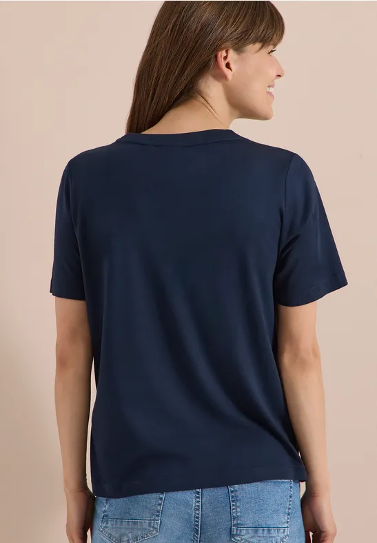 Eine Frau von hinten trägt ein schlichtes, dunkelblaues T-Shirt und Jeans.