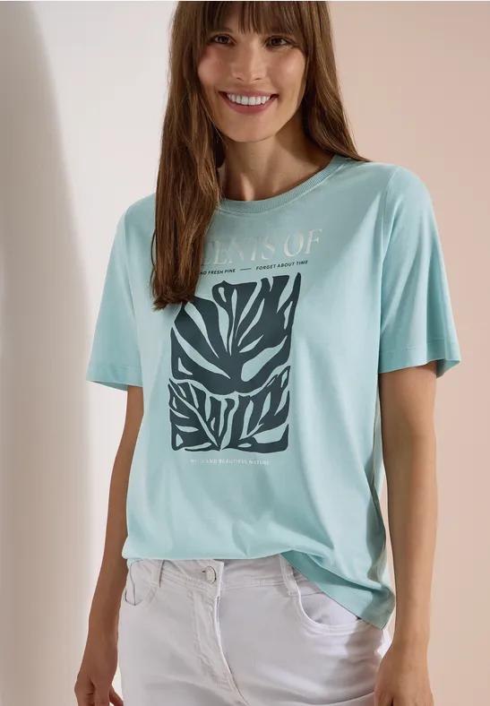 eine Frau trägt ein hellblaues T-Shirt mit Zebramuster und weiße Hose, Gesicht unscharf.