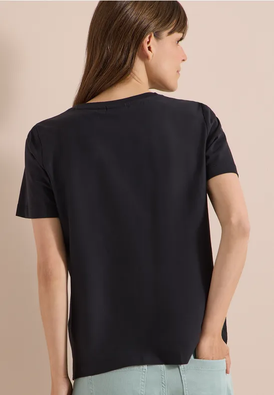 Frau in schwarzem Kurzarmshirt steht mit dem Rücken zur Kamera, der Hintergrund ist neutral.