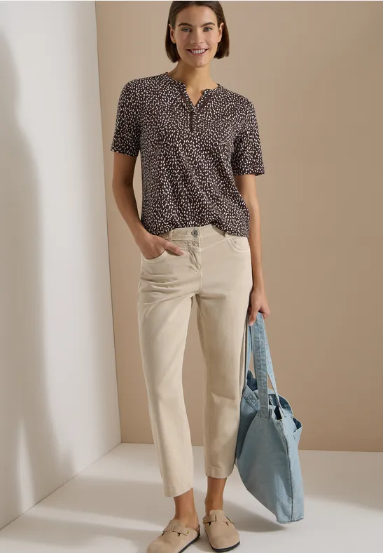 Modisches Outfit: Gemustertes Kurzarmtop, helle, gerade geschnittene Hosen und hellblaue Tasche.