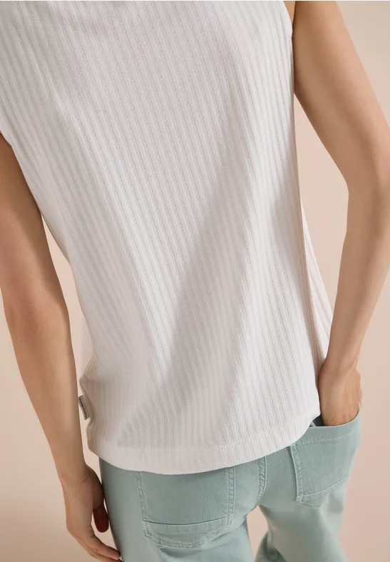 Rückenansicht einer Person in weißem, geripptem Top und hellblauen Jeans.