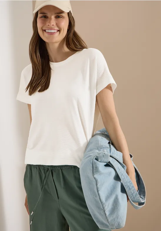 Frau in weißem T-Shirt und grüner Hose hält eine große hellblaue Tasche.