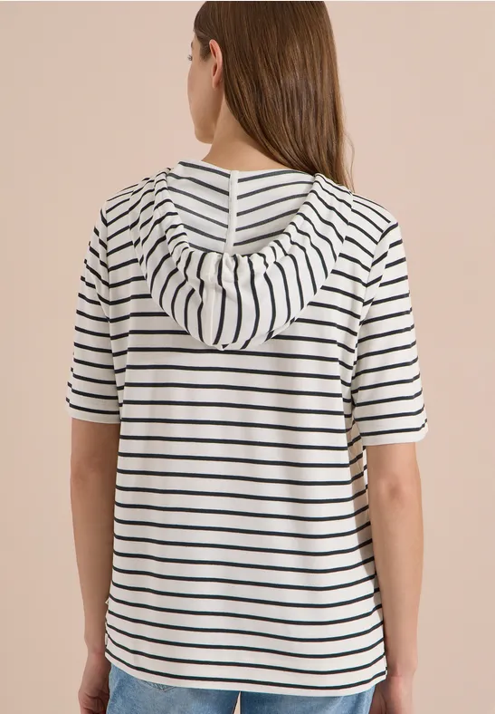 Vrouw van achteren in een wit kort capuchonshirt met zwarte strepen.