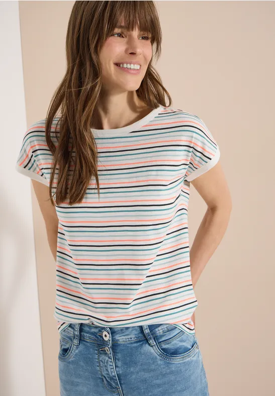 Frau in gestreiftem T-Shirt und blauer Jeans steht lässig mit den Händen am Rücken.
