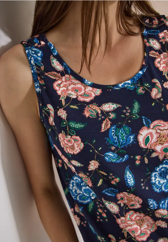 Ein ärmelloses Top mit blau-rosa Blumenmuster auf dunkelblauem Stoff, am Oberkörper einer Frau.