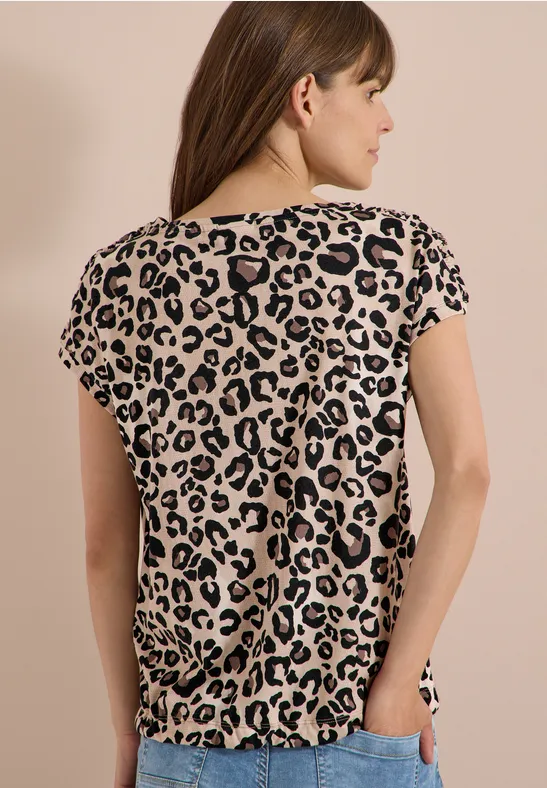 Frau von hinten in beige-schwarzem Leopardenmuster-T-Shirt vor hellem Hintergrund.