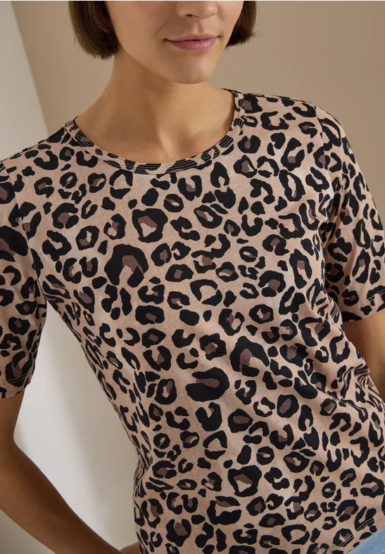 Frau mit kurzem braunem Haar trägt beiges T-Shirt mit schwarzem Leopardenmuster.