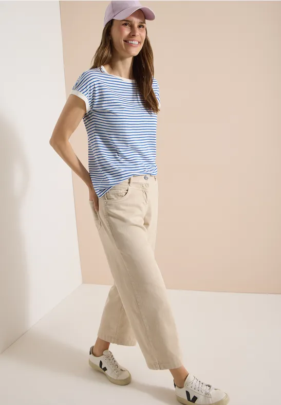 Lockeres Outfit: Gestreiftes T-Shirt, helle Culotte und weiße Sneaker vor neutralem Hintergrund.