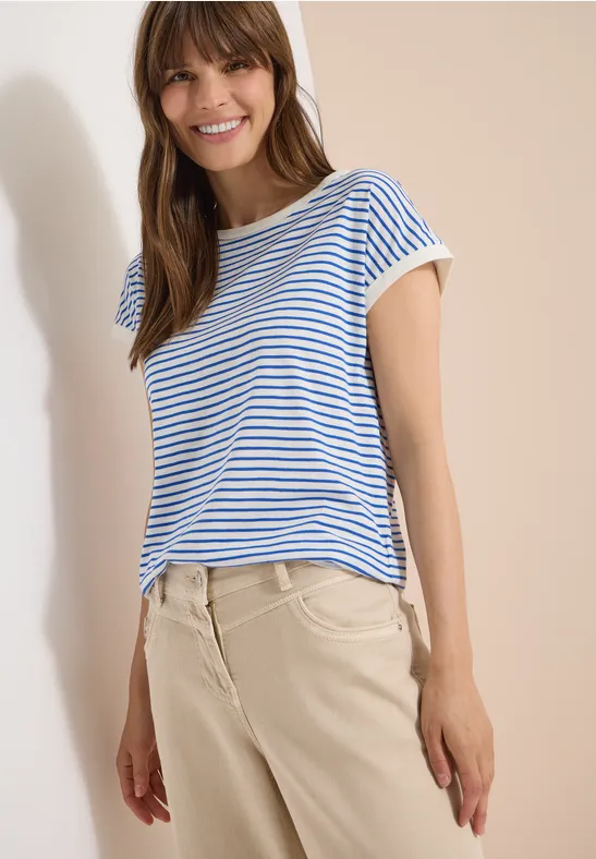 Frau trägt blau-weiß gestreiftes T-Shirt und beige Hose vor hellem Hintergrund.