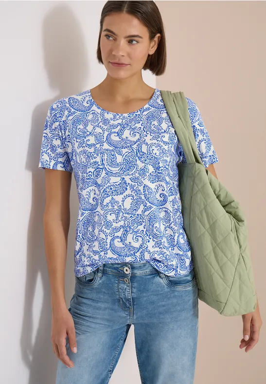Frau trägt blau-weiß gemustertes Shirt, Jeans und grüne gesteppte Tasche.