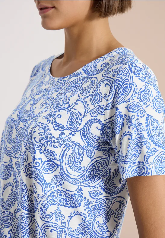Frau im Profil trägt weißes T-Shirt mit blauem Paisley-Muster.
