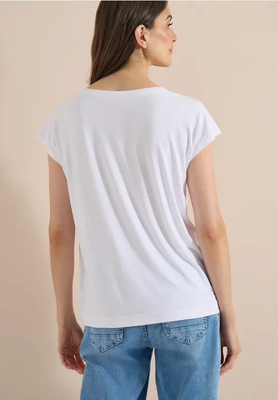 Personne vue de dos portant un t-shirt blanc et un jean bleu sur fond beige.