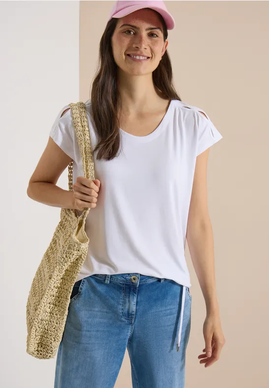 Femme en T-shirt blanc, jean bleu, casquette rose, portant un sac en paille.