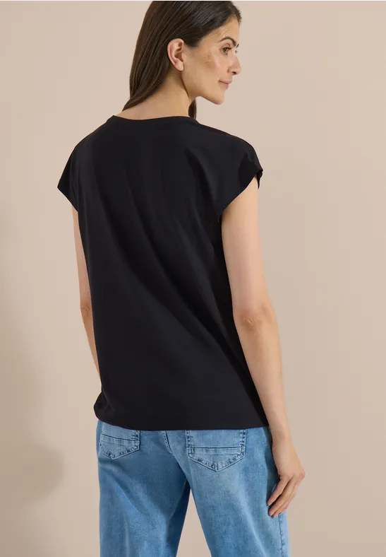 Vue de dos d'une femme portant un t-shirt noir et un jean bleu sur fond neutre.