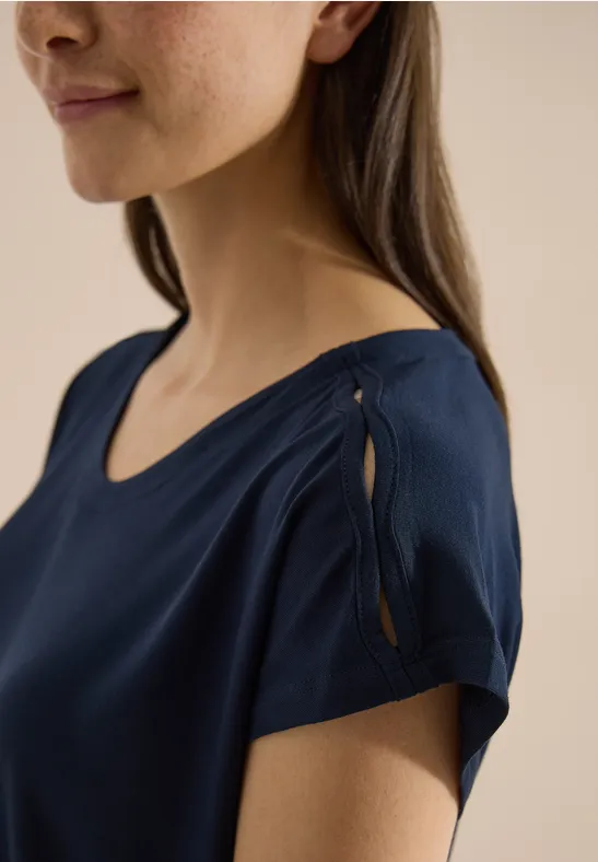 Une femme porte un haut bleu marine à manches courtes avec une fente et un détail noué à l'épaule.