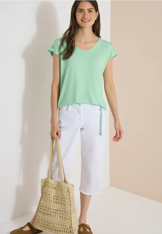 Femme en t-shirt vert menthe et pantalon blanc court, tenant un sac en paille.