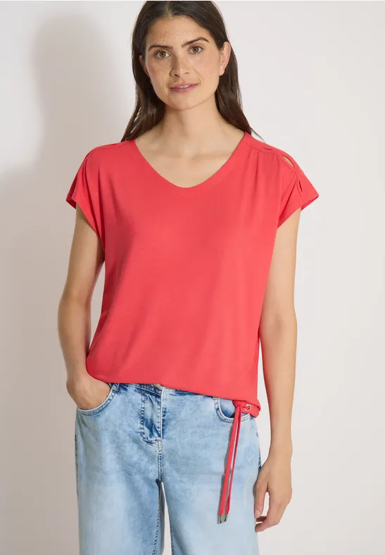 Femme décontractée portant un t-shirt rouge et un jean, mains dans les poches.