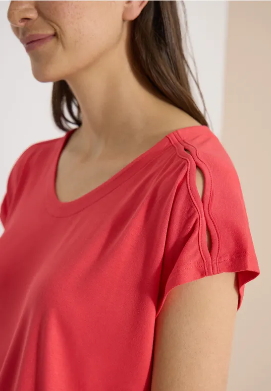 Femme en haut rouge corail avec encolure arrondie et ouverture décorative à l'épaule