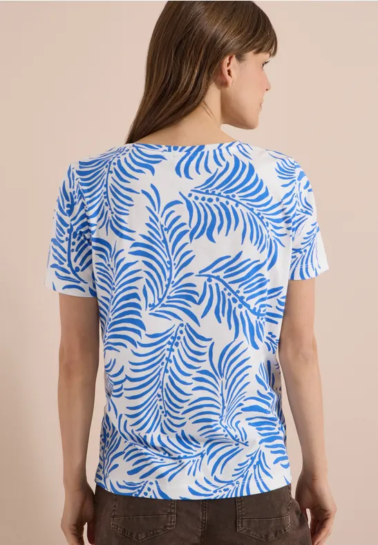 Rückansicht einer Frau in weißem Kurzarmshirt mit blauem Blattmuster.