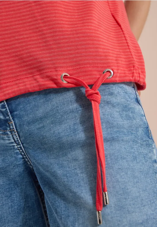 Rotes gestreiftes Shirt mit Tunnelzug-Kordel und Knoten über hellblauen Jeans.