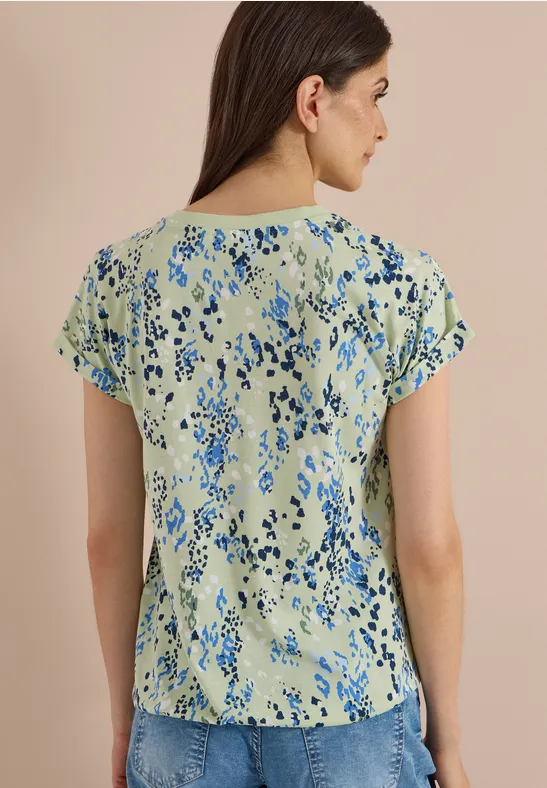 Frau von hinten in hellgrüner Bluse mit blauem Blumenmuster.