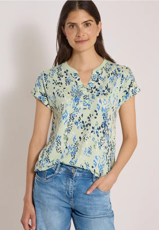 Eine Frau trägt eine hellgrüne Bluse mit Blumenmuster und blaue Jeans.