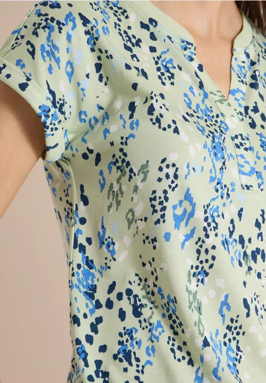 Hellgrüne Bluse mit blauem abstraktem Muster, kurzem Ärmel und kleiner Knopfleiste.