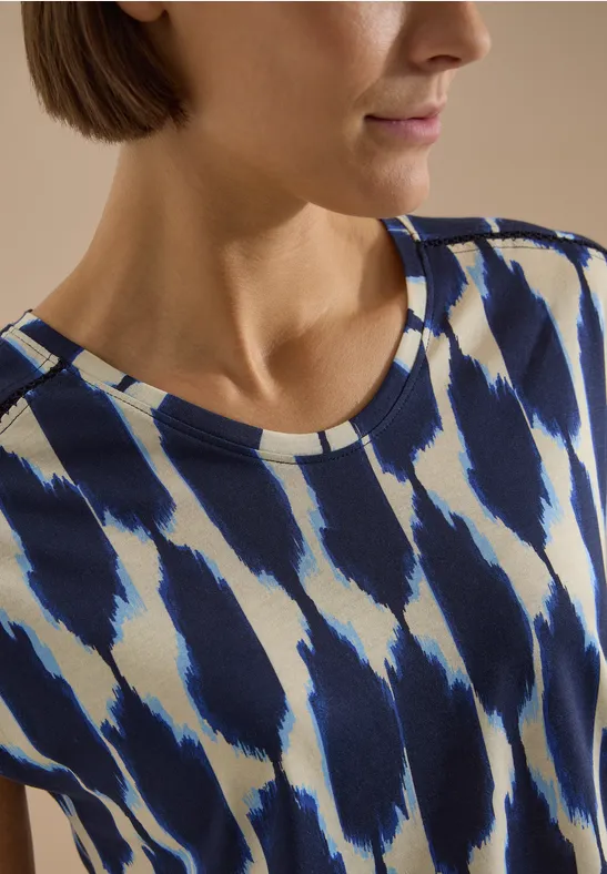 Frau trägt blau-weiß gemustertes Oberteil mit Pinselstrichdesign.